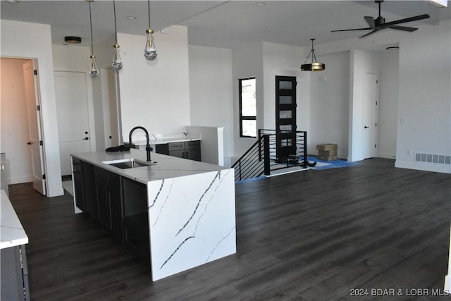 kitchen with ceiling fan, a kitchen island with sink, dark wood-type flooring, hanging light fixtures, and sink