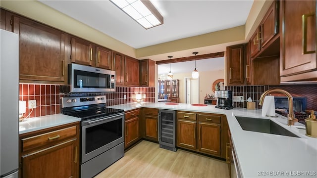 kitchen with appliances with stainless steel finishes, sink, wine cooler, decorative backsplash, and hanging light fixtures