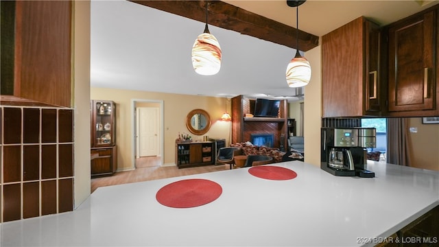 kitchen with a large fireplace, light wood-type flooring, hanging light fixtures, kitchen peninsula, and beam ceiling