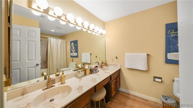 full bathroom with hardwood / wood-style flooring, vanity, shower / bath combo with shower curtain, and toilet