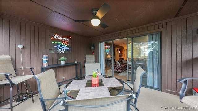 dining area with carpet flooring, a ceiling fan, and wooden walls