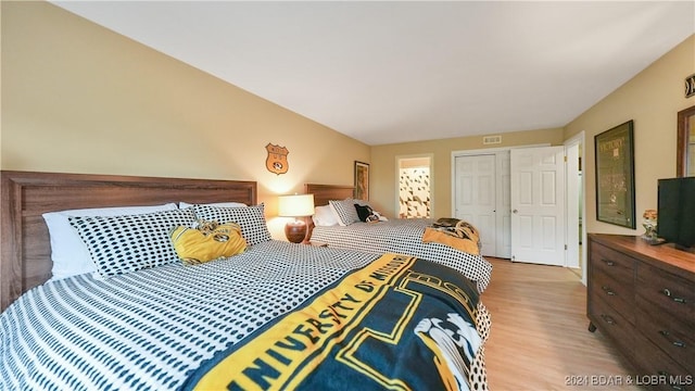 bedroom with light wood-type flooring, visible vents, and a closet