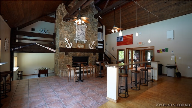 kitchen with a stone fireplace, a breakfast bar, wooden ceiling, and high vaulted ceiling