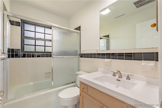 full bathroom featuring toilet, shower / bath combination with glass door, vanity, and tile walls