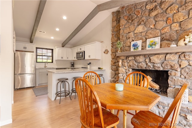 dining room with vaulted ceiling with beams, a stone fireplace, sink, and light wood-type flooring