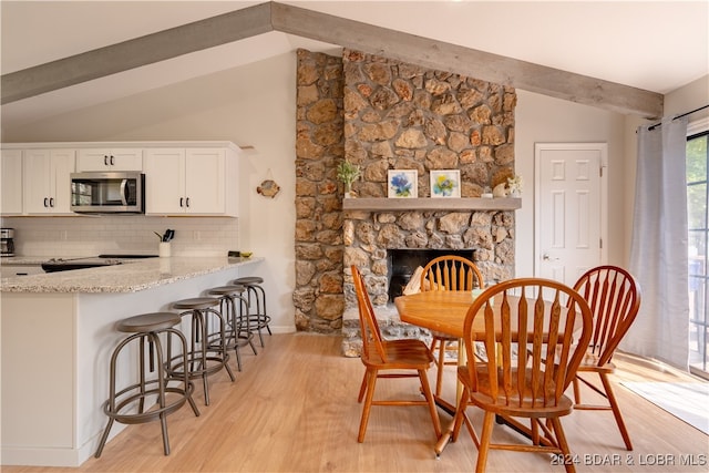 dining area featuring light hardwood / wood-style floors, lofted ceiling with beams, and a fireplace