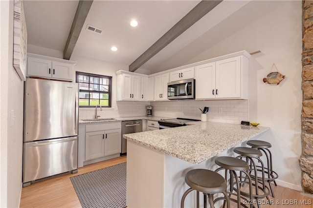 kitchen featuring light stone countertops, white cabinets, stainless steel appliances, sink, and a breakfast bar area