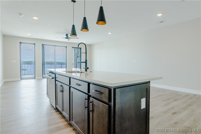 kitchen with decorative light fixtures, light wood finished floors, light countertops, open floor plan, and an island with sink