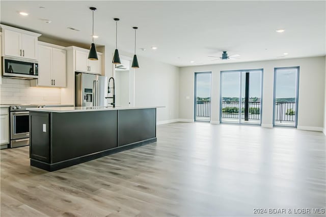 kitchen featuring light wood finished floors, appliances with stainless steel finishes, an island with sink, and baseboards