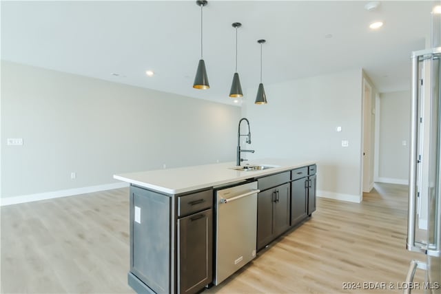 kitchen with a sink, light countertops, hanging light fixtures, dishwasher, and an island with sink