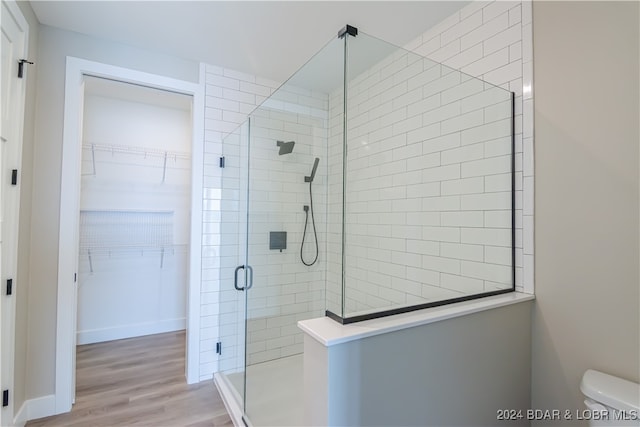 bathroom featuring toilet, a shower stall, a walk in closet, and wood finished floors