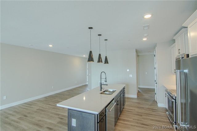 kitchen featuring white cabinets, high quality appliances, a kitchen island with sink, light countertops, and a sink