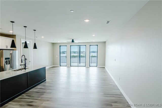 kitchen with light wood-style flooring, stainless steel fridge with ice dispenser, ceiling fan, a sink, and baseboards