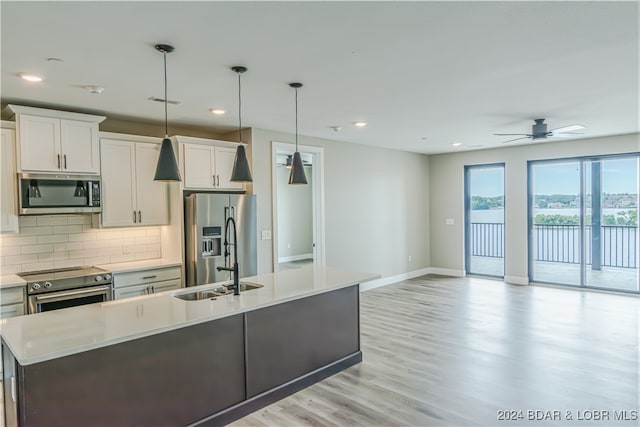 kitchen featuring a kitchen island with sink, white cabinetry, light countertops, appliances with stainless steel finishes, and decorative light fixtures