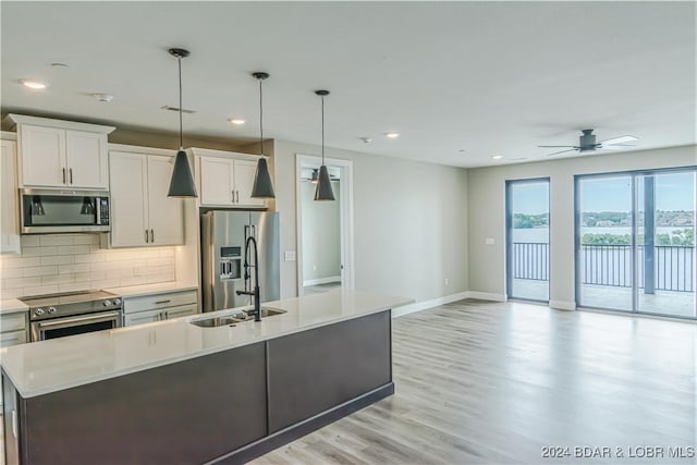kitchen with a sink, stainless steel appliances, light countertops, baseboards, and a center island with sink
