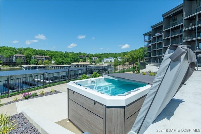 view of pool with fence, a water view, and an outdoor hot tub