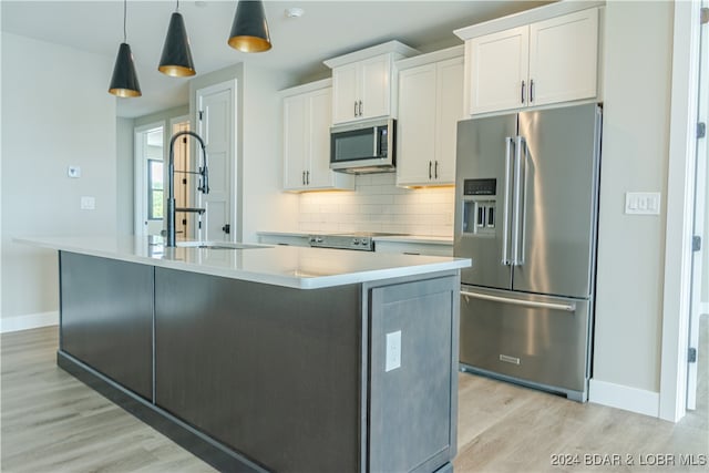 kitchen with a kitchen island with sink, stainless steel appliances, a sink, white cabinetry, and light countertops