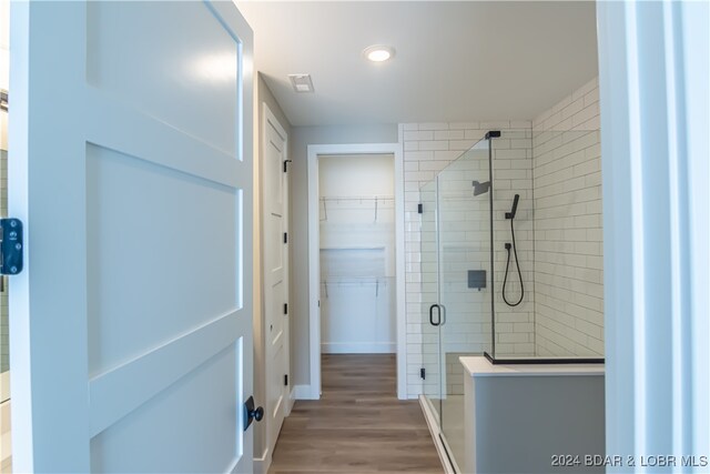 bathroom with a spacious closet, wood finished floors, a shower stall, and visible vents