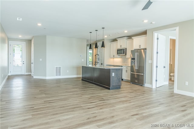 kitchen with pendant lighting, a center island with sink, stainless steel appliances, open floor plan, and white cabinetry