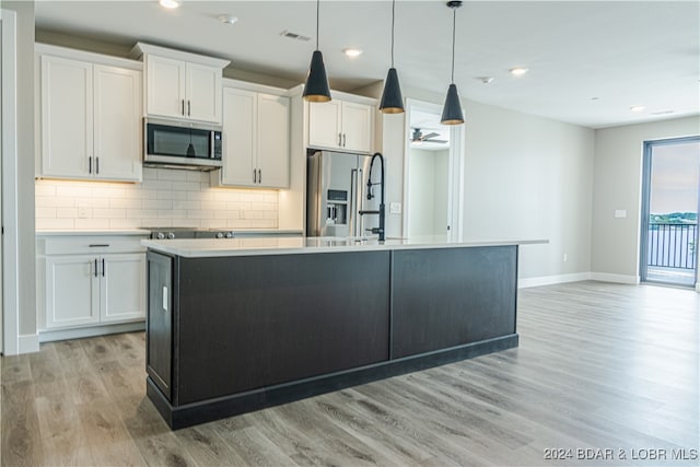 kitchen with stainless steel appliances, white cabinets, hanging light fixtures, light countertops, and an island with sink