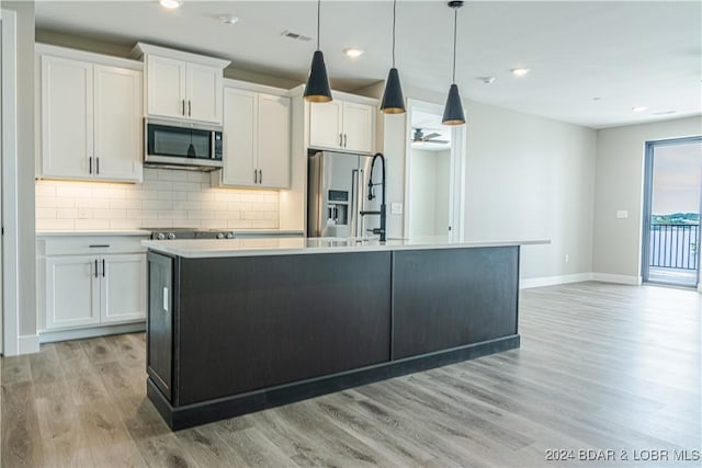 kitchen featuring white cabinets, an island with sink, stainless steel appliances, and baseboards