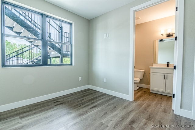 unfurnished bedroom featuring ensuite bath, light wood-style flooring, and baseboards