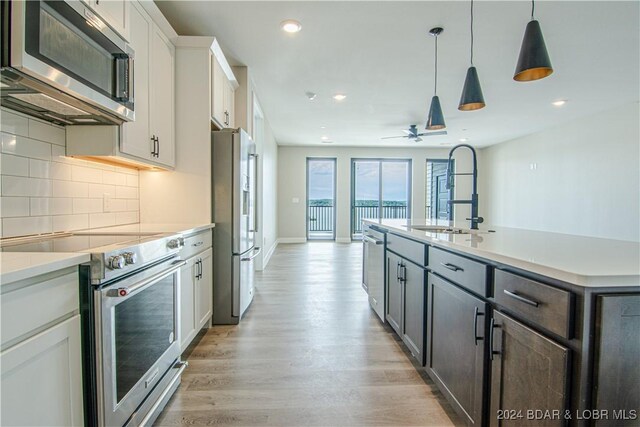 kitchen featuring a sink, stainless steel appliances, tasteful backsplash, light wood-style flooring, and light countertops