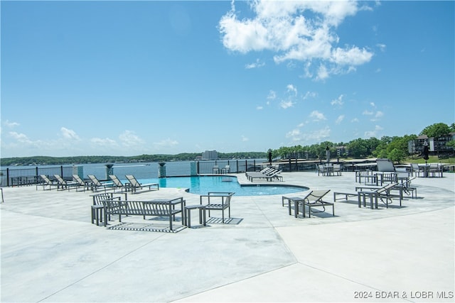 pool featuring a patio, a water view, and fence