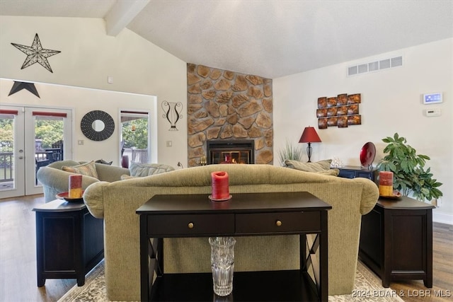 living room featuring vaulted ceiling with beams, french doors, light hardwood / wood-style floors, a fireplace, and a textured ceiling