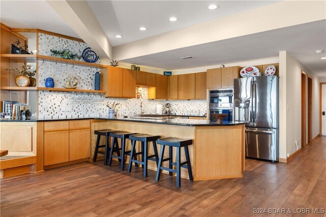 kitchen featuring appliances with stainless steel finishes, decorative backsplash, dark hardwood / wood-style flooring, and kitchen peninsula