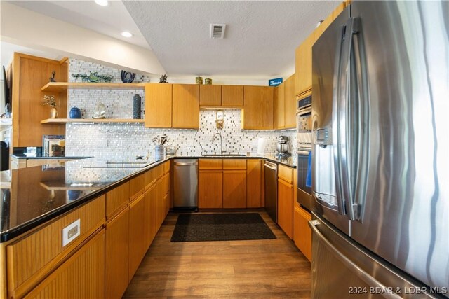 kitchen featuring dark hardwood / wood-style flooring, tasteful backsplash, stainless steel appliances, sink, and dark stone countertops