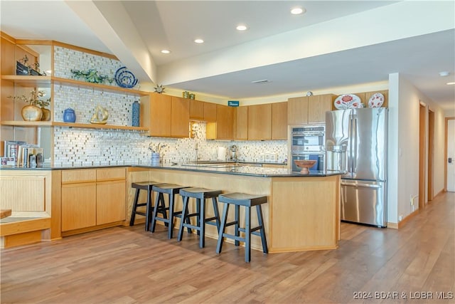 kitchen featuring stainless steel appliances, light brown cabinetry, light wood finished floors, a kitchen bar, and tasteful backsplash