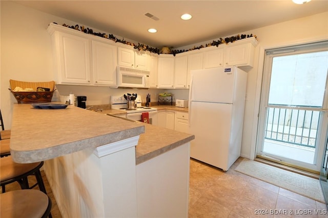 kitchen with a peninsula, white appliances, white cabinetry, light countertops, and a kitchen bar