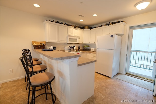 kitchen with white cabinetry, white appliances, a kitchen breakfast bar, and kitchen peninsula