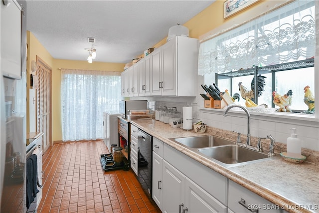 kitchen featuring sink, dishwashing machine, decorative backsplash, a textured ceiling, and white cabinets