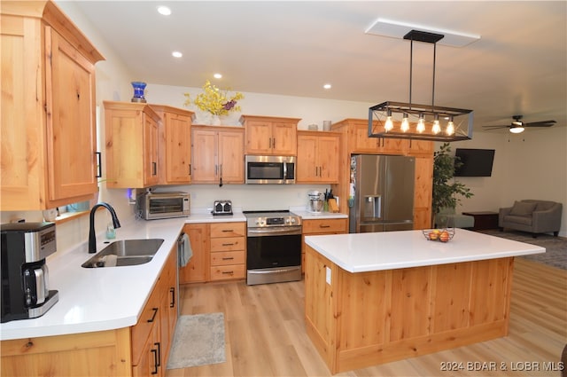 kitchen featuring sink, light wood-type flooring, appliances with stainless steel finishes, decorative light fixtures, and a kitchen island