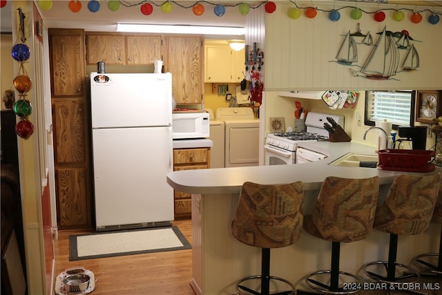 kitchen with light hardwood / wood-style flooring, a breakfast bar, sink, kitchen peninsula, and white appliances