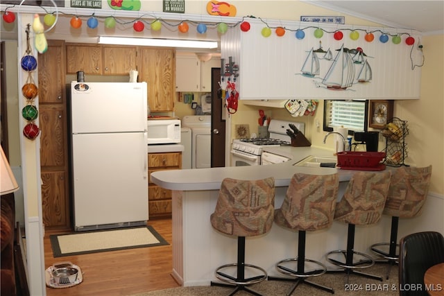 kitchen featuring sink, washing machine and clothes dryer, light wood-type flooring, kitchen peninsula, and white appliances