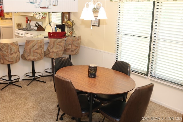 dining room with sink, light carpet, washer / clothes dryer, and a chandelier