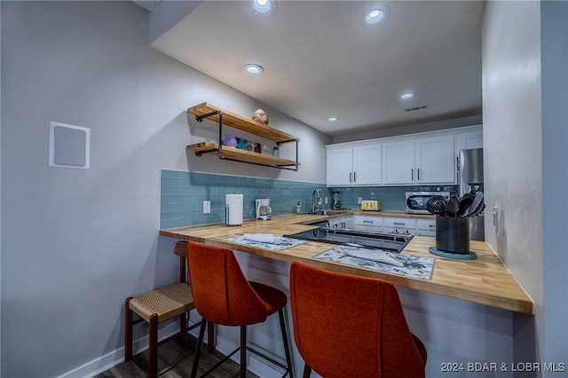 kitchen featuring tasteful backsplash, wood counters, a kitchen breakfast bar, white cabinets, and kitchen peninsula