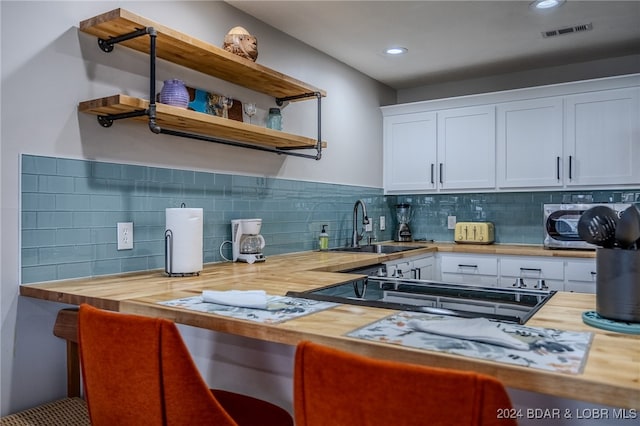 kitchen with wooden counters, backsplash, sink, and white cabinets