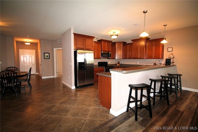 kitchen with a kitchen breakfast bar, pendant lighting, appliances with stainless steel finishes, dark wood-type flooring, and kitchen peninsula