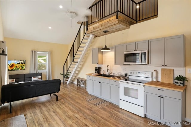 kitchen with white electric range, butcher block countertops, a sink, stainless steel microwave, and pendant lighting