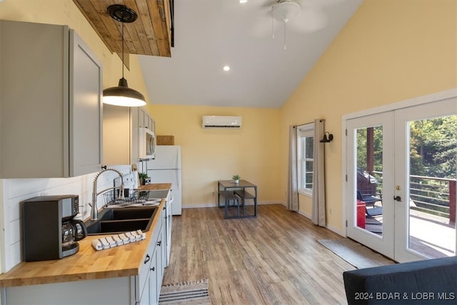 kitchen with a wall unit AC, white appliances, a sink, wooden counters, and decorative light fixtures