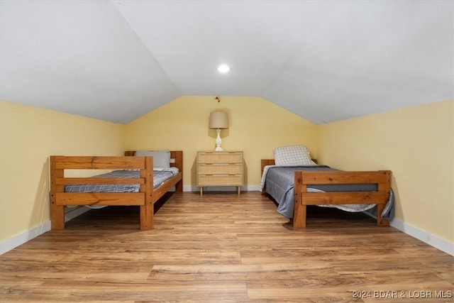 bedroom with light wood-type flooring, vaulted ceiling, and baseboards