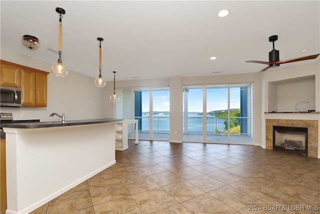 kitchen with ceiling fan, sink, a tile fireplace, and a water view