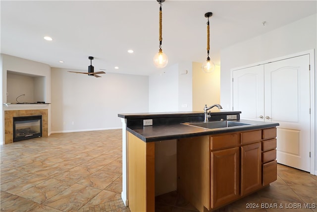 kitchen with a tile fireplace, sink, an island with sink, ceiling fan, and pendant lighting