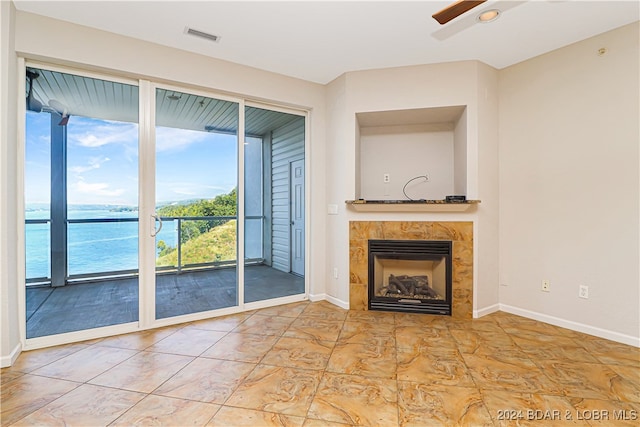 unfurnished living room featuring ceiling fan, a tiled fireplace, and a water view