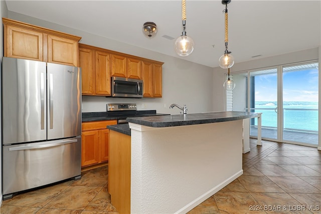 kitchen featuring an island with sink, hanging light fixtures, stainless steel appliances, sink, and a water view