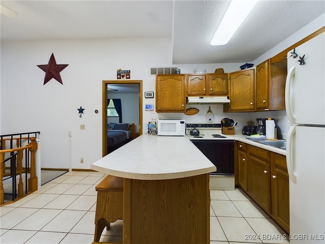 kitchen with white appliances, a textured ceiling, light tile patterned floors, and a breakfast bar area